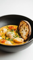 Bouillabaisse served in a sleek black bowl, paired with a rustic piece of toasted bread on the side.