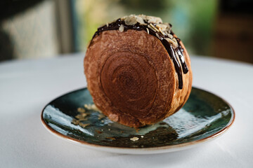 new york roll, croissant pastry dough with chocolate topping, creamy inside, cryspy textured backery served on ceramic contemporary plate, topped with glaze and hazel nuts