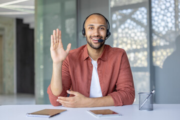 A confident businessman wearing a headset engages in an online meeting. Sitting at a desk with a...