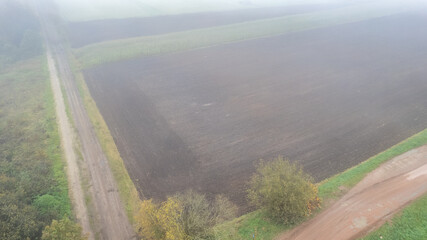 A mesmerizing misty landscape presents an expanse of vast agricultural fields along with a nearby dirt road