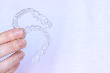 Hand holding Invisalign transparent braces on white background with copy space. Invisible retainers and aligners