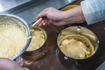 The process of making a tart or sweet pie. The confectioner's hands put the dough and filling in baking molds on the production table.