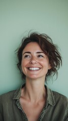 Fototapeta premium A joyful woman with short hair smiles radiantly, standing in front of a pastel green background, conveying happiness and contentment.