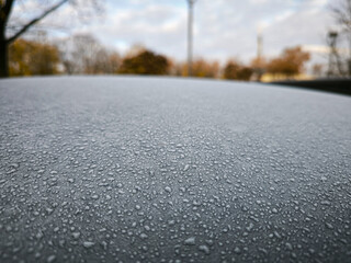 A car's hood is covered in raindrops. Concept of cold and wetness, as well as the idea of a rainy day.