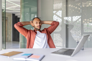 A relaxed business professional sits back in an office, enjoying a moment of rest. With his laptop...