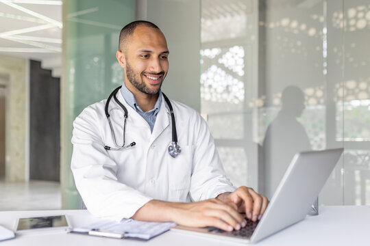 A smiling doctor is using a laptop in a modern office setting, showcasing productivity and professionalism. The image captures a sense of technology integration in the healthcare field.