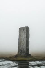 A solitary stone monolith stands amidst a foggy landscape.