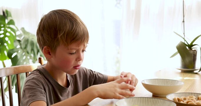 Young boy sitting at a table shows a disgusted expression while refusing to eat a boiled egg served in a bowl, highlighting the challenges of picky eating during breakfast
