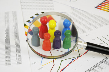 People in economy concept. Colored wooden people figures under magnifying glass on financial report.