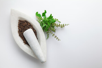 Close-up of fresh organic green Holy Basil or Rama Tulsi (Ocimum sanctum) leaves alongside its dried leaves, placed on a white marble mortar and pestle, isolated on a white background.