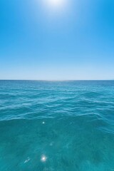 Obraz premium The ocean is calm and clear, with a bright blue sky above. The water is a deep shade of blue, and the sun is shining brightly, creating a peaceful and serene atmosphere