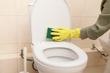 Home Cleaning in Protective Yellow Gloves, Green sponge. Cleans Toilet