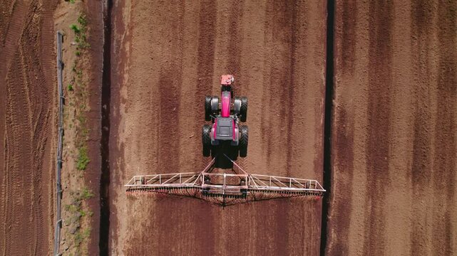 Aerial top down tracking follows tractor heavy machinery processing a peat field with visible parallel rows and rural surroundings