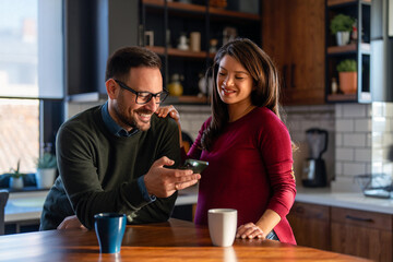 Happy pregnant woman and her husband making selfie, surfing internet, having fun with gadgets