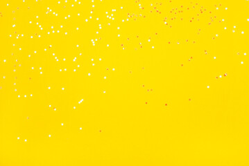 Tiny pearl stars on yellow background. Flat lay, top view.