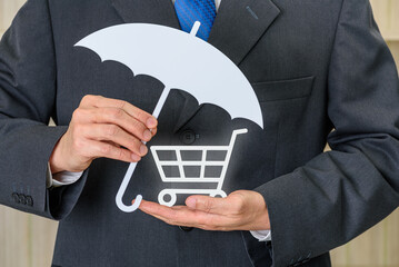 "Consumer protection law and business transactions." The businessman holding an umbrella over a shopping cart signifies financial protection, insurance for purchases, and trust in trade practices.