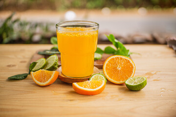 A glass of freshly squeezed orange juice on a wooden table surrounded by orange slices and orange leaves