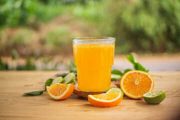 A glass of freshly squeezed orange juice on a wooden table surrounded by orange slices and orange leaves