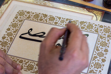 Close-up of a calligraphist writing an Arabic name for a customer in Arabic calligraphy with ink.