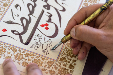 Close-up of a calligraphist writing an Arabic name for a customer in Arabic calligraphy with ink.