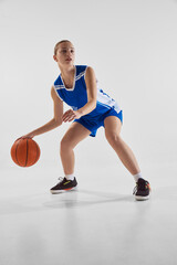 Concentrated young teen girl, basketball player in blue uniform in motion with ball during game,...