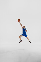 Slam dunk. Full-length vertical image of young teen girl in blue uniform, basketball player in...