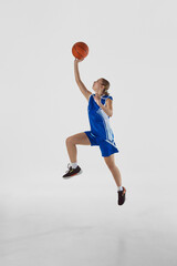 Slam dunk. Full-length vertical image of young teen girl in blue uniform, basketball player in...