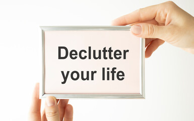 Woman hands holding cardboard card with words Declutter Your Life made by black alphabet stamps.
