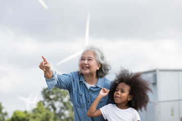 Asian grandma playing with African American mixed race girl at wind turbines farm station on...