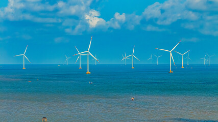 Tall windmill turbines against a clear blue sky, generating renewable energy in the serene Go Cong, Vietnam landscape by the sea. Like windmill park Westermeerdijk in the Noordoostpolder Netherlands.