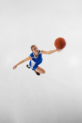 Slam dunk. Top view dynamic image of young focused teen girl in blue uniform, basketball player in...