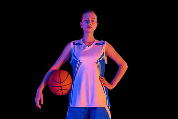 Portrait of confident teen girl, basketball player proudly standing and posing with ball against black studio background in neon light. Concept of sport, youth, motion, healthy lifestyle © master1305