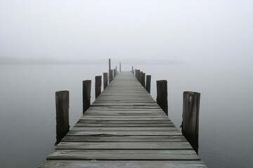Naklejka premium Weathered wooden pier leading into a misty sea the distant horizon obscured by thick fog with soft waves gently crashing against the wooden beams of the pier