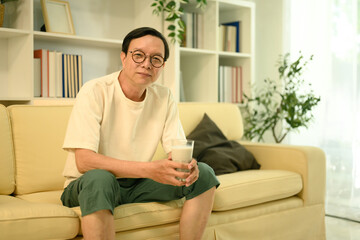 Obraz premium Relaxed middle aged man wearing casual clothes sitting on couch with a glass of milk in hand