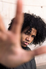 serious african american teen male with curly hair spreading hand towards camera and protesting,...