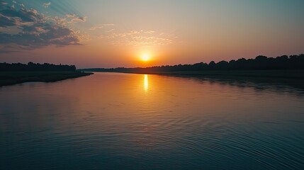 Obraz premium Serene sunset over calm river reflecting golden light.