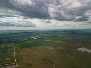 Suburban settlements on the plain. A village seen from above from the drone. Houses gathered on the vast plain cultivated by farmers with various cereals in the spring season