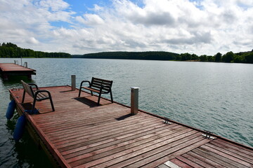 Naklejka premium A view of a wooden pier, marina or jetty located next to a vast yet shallow river covered with reeds, lilly pads and other flora with numerous boats and ships moored and swimming along the reservoir