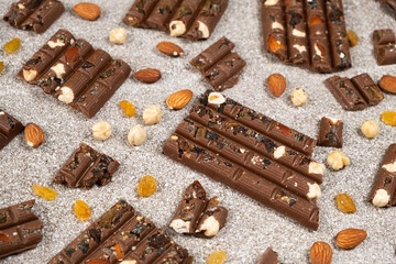 Broken chocolate pieces with nuts and raisins on a stone background