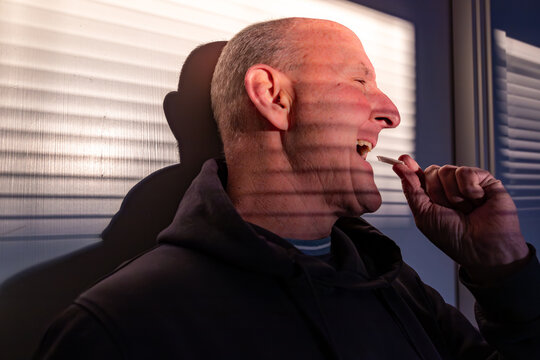 Stockholm, Sweden A middle-aged man stands in the shadow of window blinds against a wall in the sunshine and puts a tobacco-free nicotine pouch in his mouth.