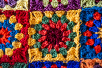 Square motif crocheted from wool yarn in burgundy, yellow, green, and red colors.