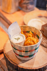 High angle, Deep-fried curly fries with dipping cheese sauce in small woven basket