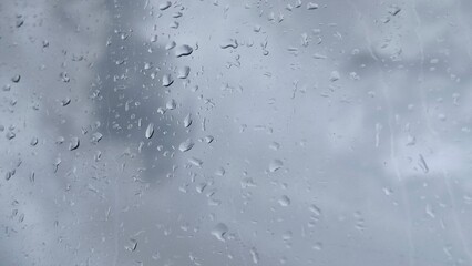 Rainwater or dew drops on wet transparent car glass window or windshield surface with dark cloud sky background. Rainy season, condensation, spring, storm, rainfall, cloudscape and typhoon concept.