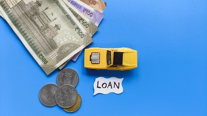 Car loan creative concept. Toy car vehicle on blue table background near Indian rupee bank currency notes and coins with copy space. Car loan word or text written on white paper.