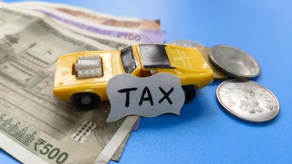 Luxury passenger car tax creative concept. Toy car vehicle on blue table background near Indian rupee bank currency notes and coins with copy space. Car tax word or text written on white paper.