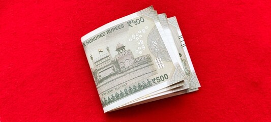 A bundle of folded five hundred Indian rupee bank paper currency notes on red table background. Extreme closeup macro flat lay top view. India inflation, tax, salary, income, EMI, and loan concept.