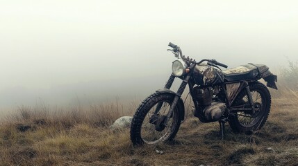 A rugged stock motorbike with a frayed seat cover and dented side panel, on a misty hillside,