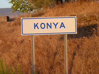 Blue 'Konya' Sign on a Metal Pole: A Bold Contrast Against the Natural Landscape of Brown Grass and Soft Shadows, Capturing a Serene Afternoon in the Heart of the City.