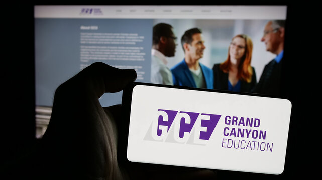 Stuttgart, Germany - 11-14-2024: Person holding mobile phone with logo of US company Grand Canyon Education Inc. (GCE) on screen in front of web page. Focus on phone display.