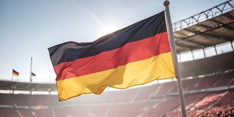germany flag waving in the wind against a sunny sky, with a blurred stadium in the background